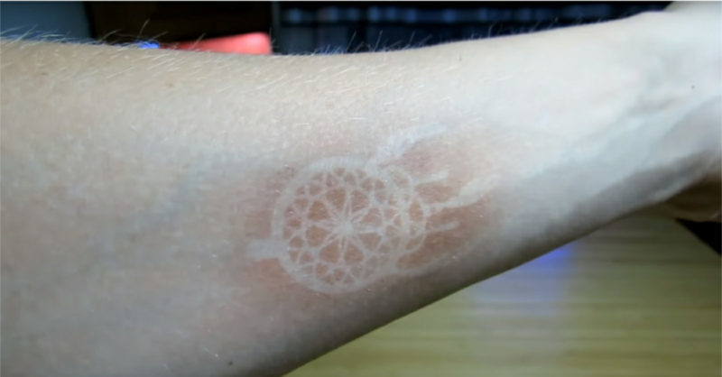 A kísérlet eredménye. Leégés egy tucat ötperces besugárzás után, hagyományos, 365 nm hullámhosszú ultraibolya zseblámpával, mintás stencilen keresztül.